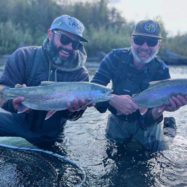 Two fly fishermen holding large rainbow trout in a Northern California river, wearing Taco Fly Co gear during a guided fishing trip